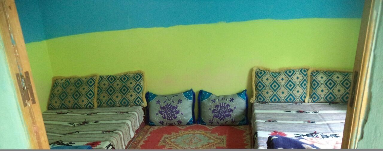 A room with two beds, each with patterned bedding and pillows. The walls are painted in two colors, and there is a visible door frame on the left.