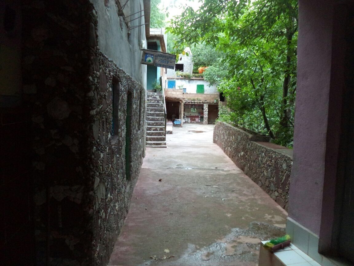 A narrow alleyway with stone walls, a concrete path, and a staircase leading to a building.