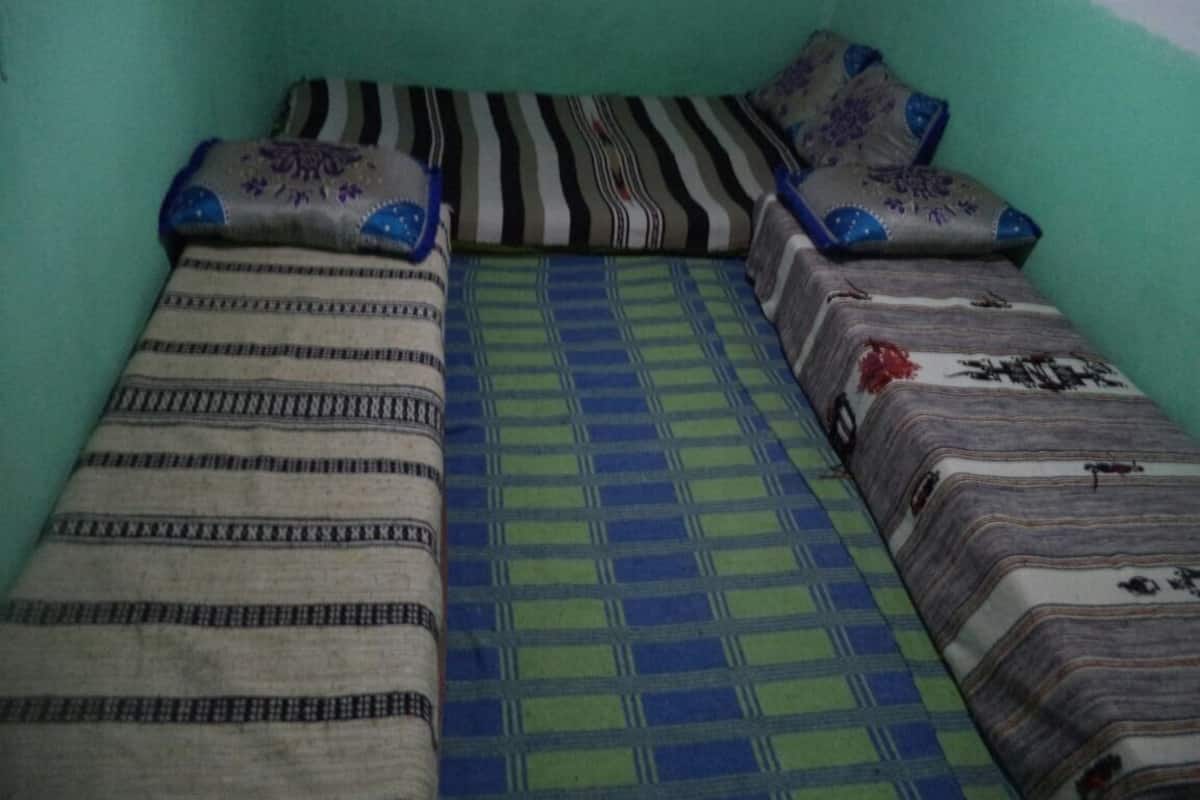 A small, single-bed room with a green wall and patterned bedding.