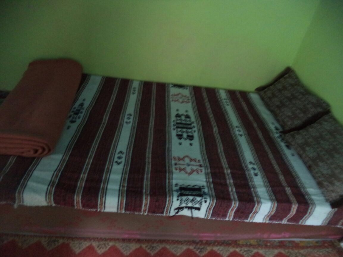 A bed with a striped bedspread and a rolled-up blanket.