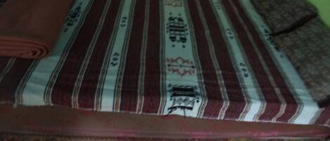 A bed with a striped bedspread and a rolled-up blanket.