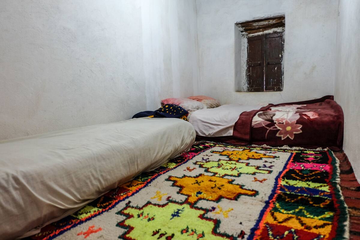 Una habitación pequeña y estrecha con dos camas individuales y un tapete colorido.