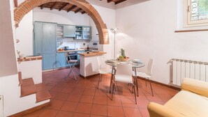 Una cocina compacta con un arco de ladrillo, un comedor con mesa de vidrio y un sofá color beige.