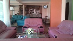 A living room with two pink sofas, a glass coffee table with a magazine, and a floral centerpiece. - Zenith Hotel Kigali (Kigali)