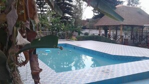 A swimming pool with a tiled deck, surrounded by tropical plants and a gazebo. - Zenith Hotel Kigali (Kigali)