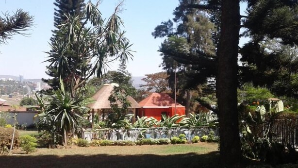 A residential area with a red house surrounded by tropical vegetation and a thatched-roof structure. - Zenith Hotel Kigali (Kigali)