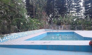 A swimming pool with a tiled edge, surrounded by dense foliage and a metal fence. - Zenith Hotel Kigali (Kigali)