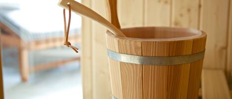 A wooden bucket with metal bands and a wooden handle, placed on a wooden stand.