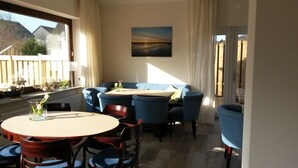 A dining area with a round table and blue chairs, a window with curtains, and a painting on the wall. - Hotel Jess am Meer (Büsum)