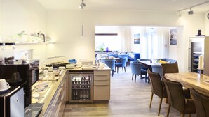 A modern hotel lobby with a coffee station, seating area, and a view of the city. - Hotel Jess am Meer (Büsum)