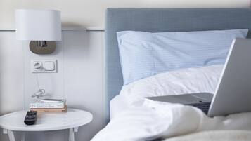 En pænt redt seng med en bærbar computer, en sengetlampe og en fjernbetjening på et lille hvidt bord ved siden af.