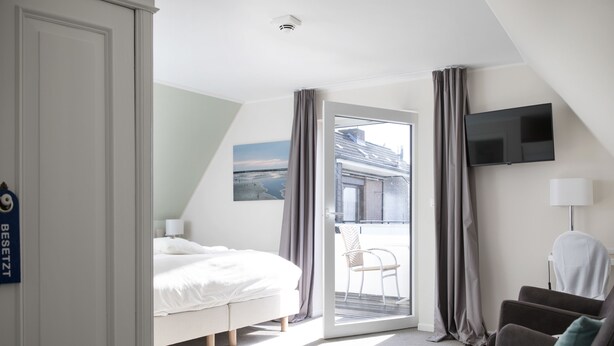 A hotel room with a bed, a chair, a television, and a view of the outside. - Hotel Jess am Meer (Büsum)