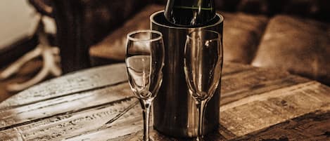 A bottle of champagne in a metallic holder on a wooden table, accompanied by two wine glasses.