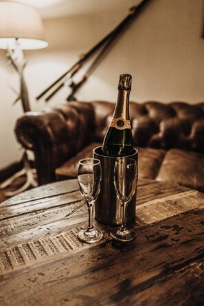 Una botella de champán en un porta champán metálico sobre una mesa de madera, junto a dos copas de vino.