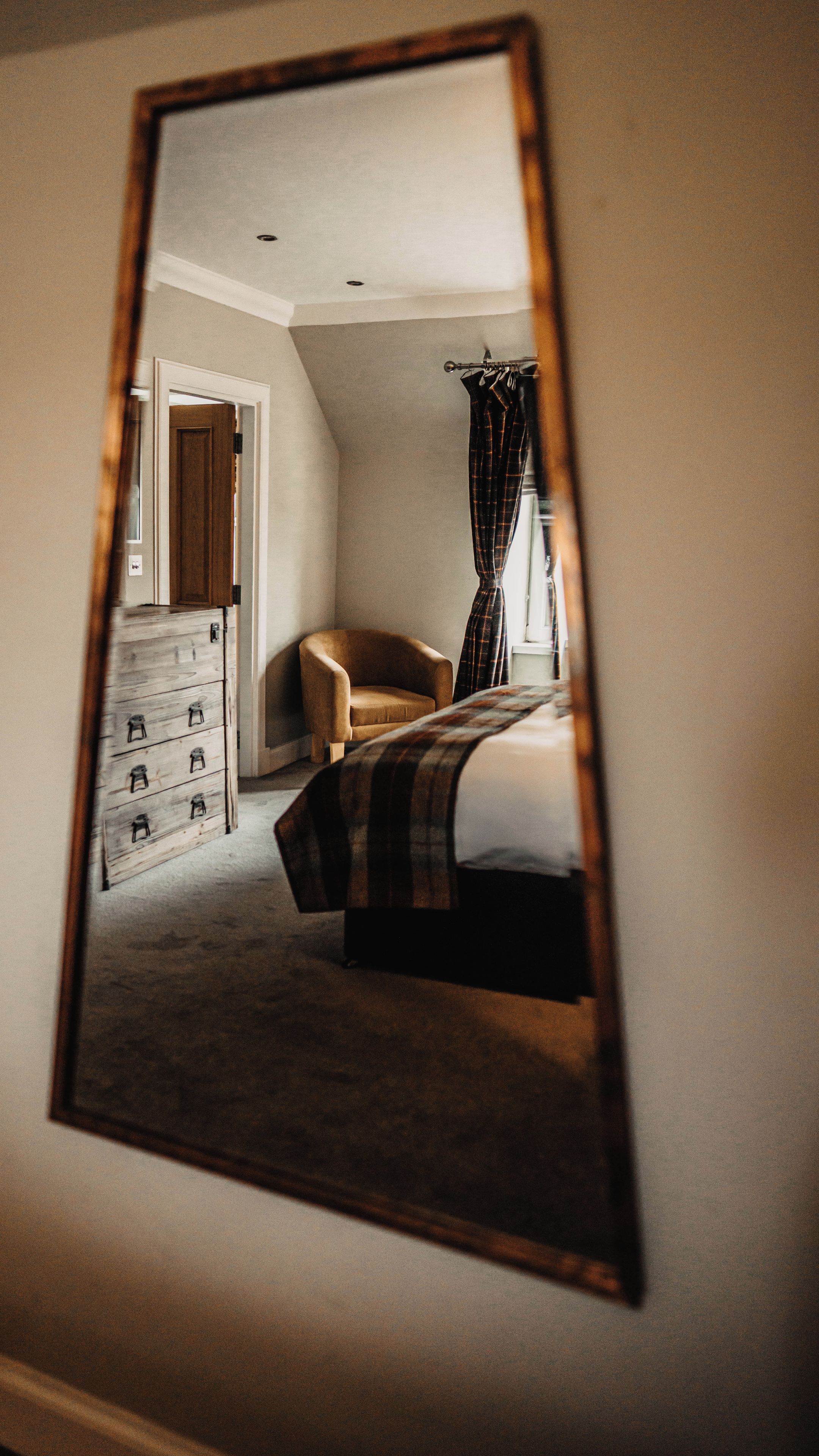 Una camera da letto con un letto, una sedia, una cassettiera e uno specchio che riflette l'ambiente.