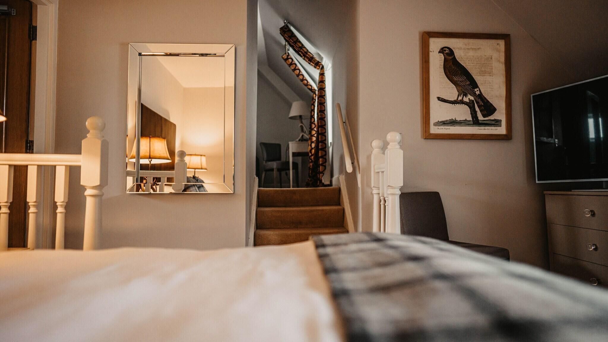 Hotelkamer met een bed, een spiegel, een vogelafbeelding in een lijst, een trap en een televisie.