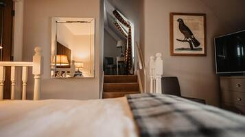 Hotelkamer met een bed, een spiegel, een vogelafbeelding in een lijst, een trap en een televisie.