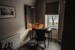 Una habitación con escritorio, silla, radiador, ventana y un cuadro en la pared.