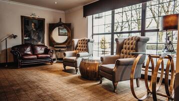 A room with a large window, a leather sofa, two armchairs, a wooden coffee table, and a lamp.
