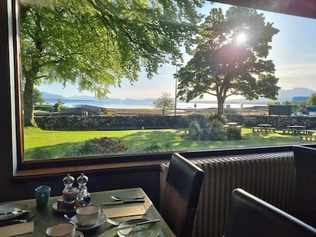 A dining area with a table set for two, a view of a landscaped garden, and a large tree in the background.