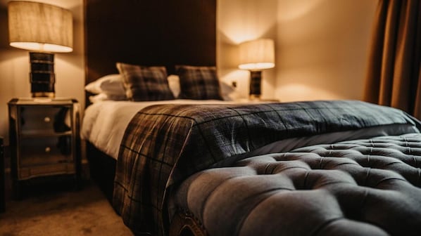 A neatly made bed with a plaid bedspread and a tufted headboard, flanked by two bedside tables with lamps.