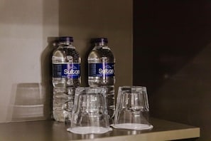 To vandflasker og tre tomme glas på en hylde.
