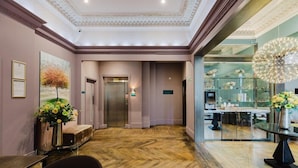 A hotel lobby with a herringbone floor, an elevator, a reception desk, and a glass display case with flowers. - Arbor Hyde Park (London)