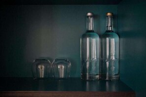 Três garrafas de vidro e dois vasos de vidro sobre uma superfície de madeira, contra um fundo escuro.