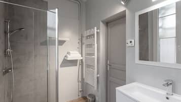 Une salle de bain moderne avec une douche à parois de verre, un meuble-lavabo blanc avec un miroir et un porte-serviettes.