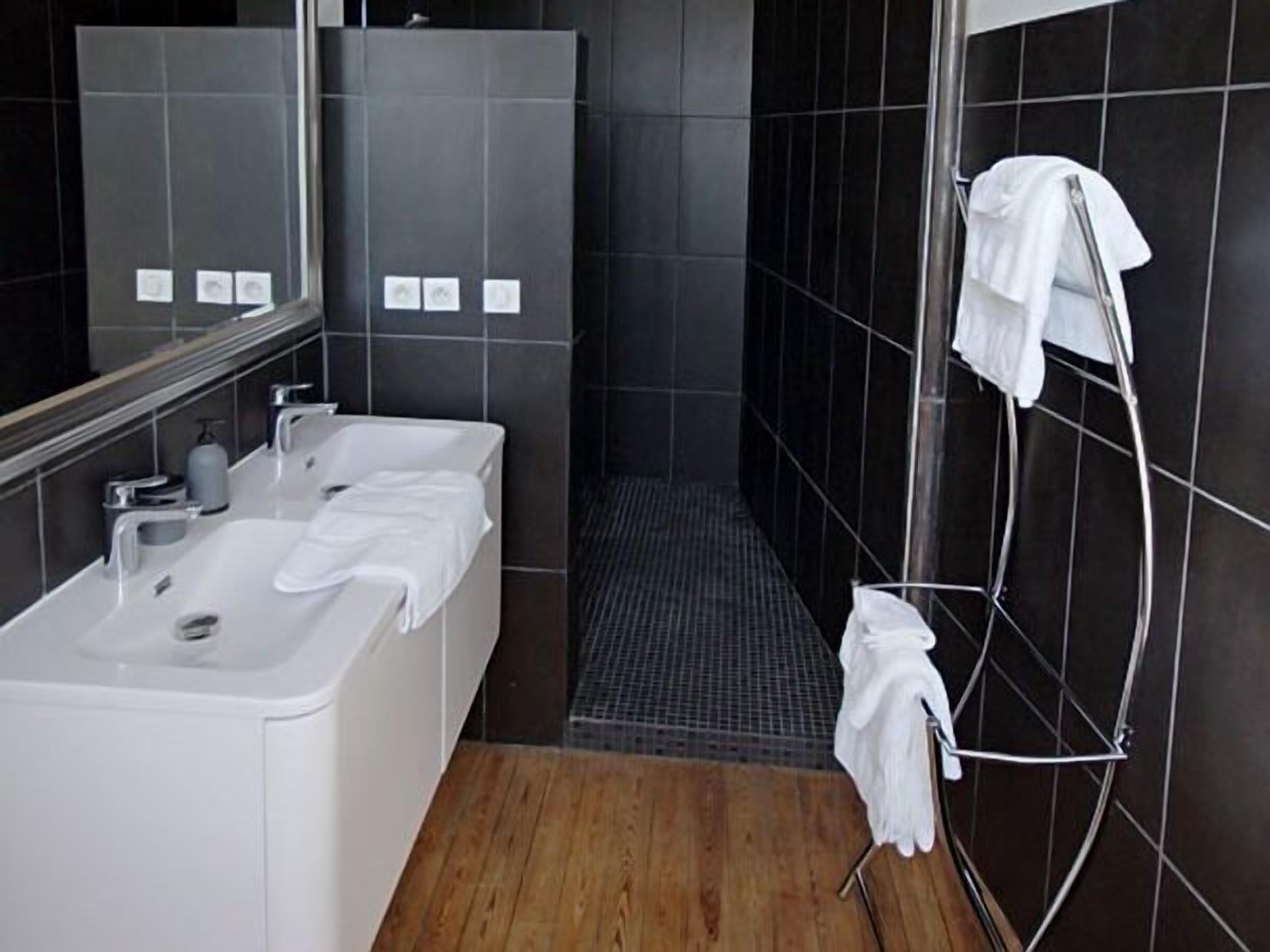 Un baño moderno con un lavabo blanco, dos espejos, zona de ducha y un perchero para toallas.