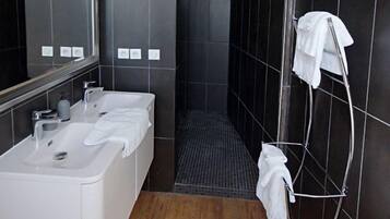 Un baño moderno con un lavabo blanco, dos espejos, zona de ducha y un perchero para toallas.