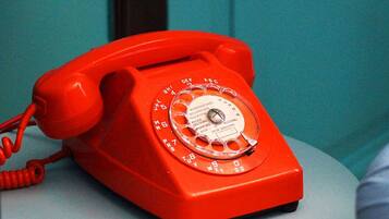 A red rotary dial telephone on a table.