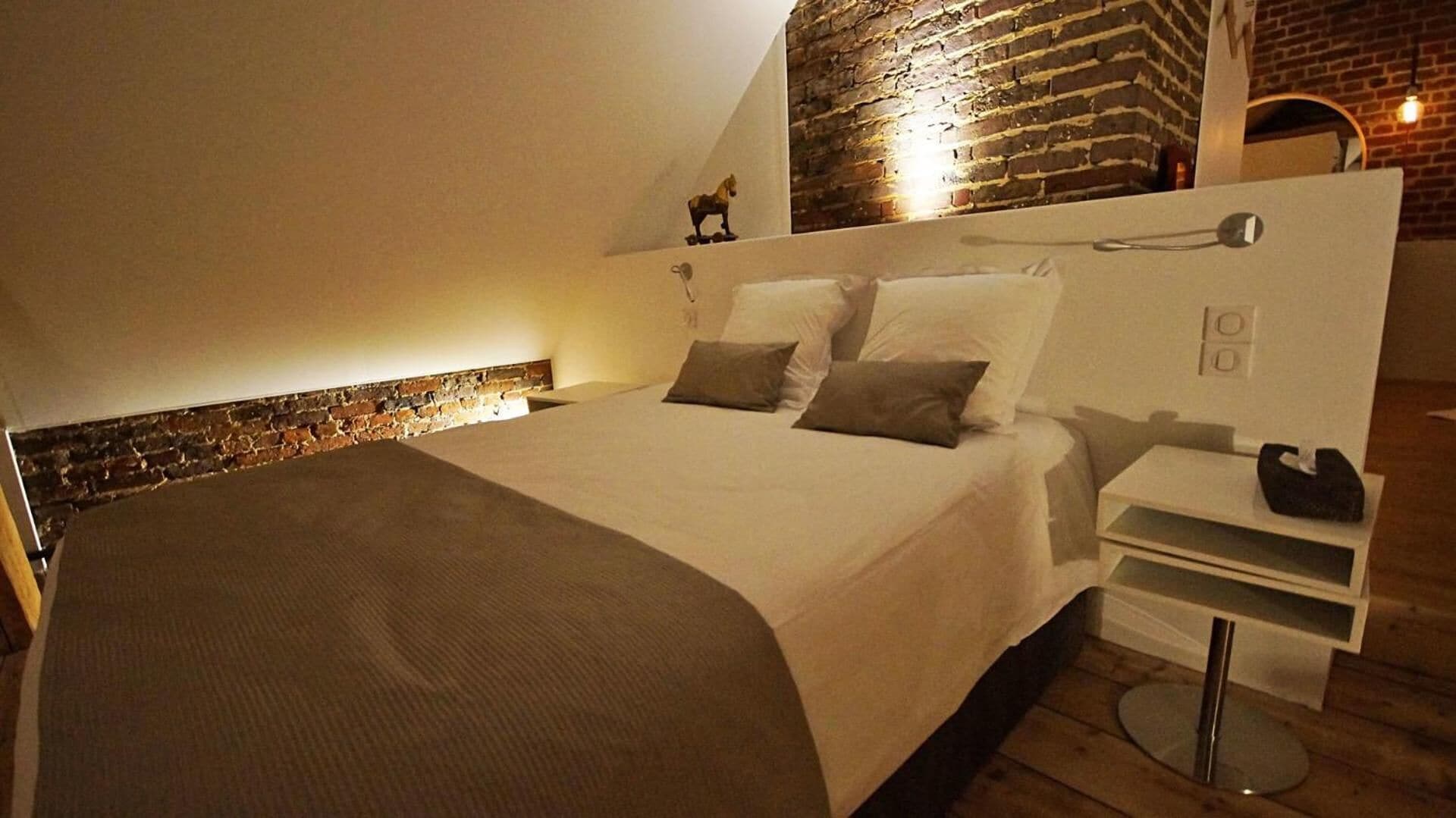 A bedroom with a bed, a nightstand, a brick wall, and a small statue.