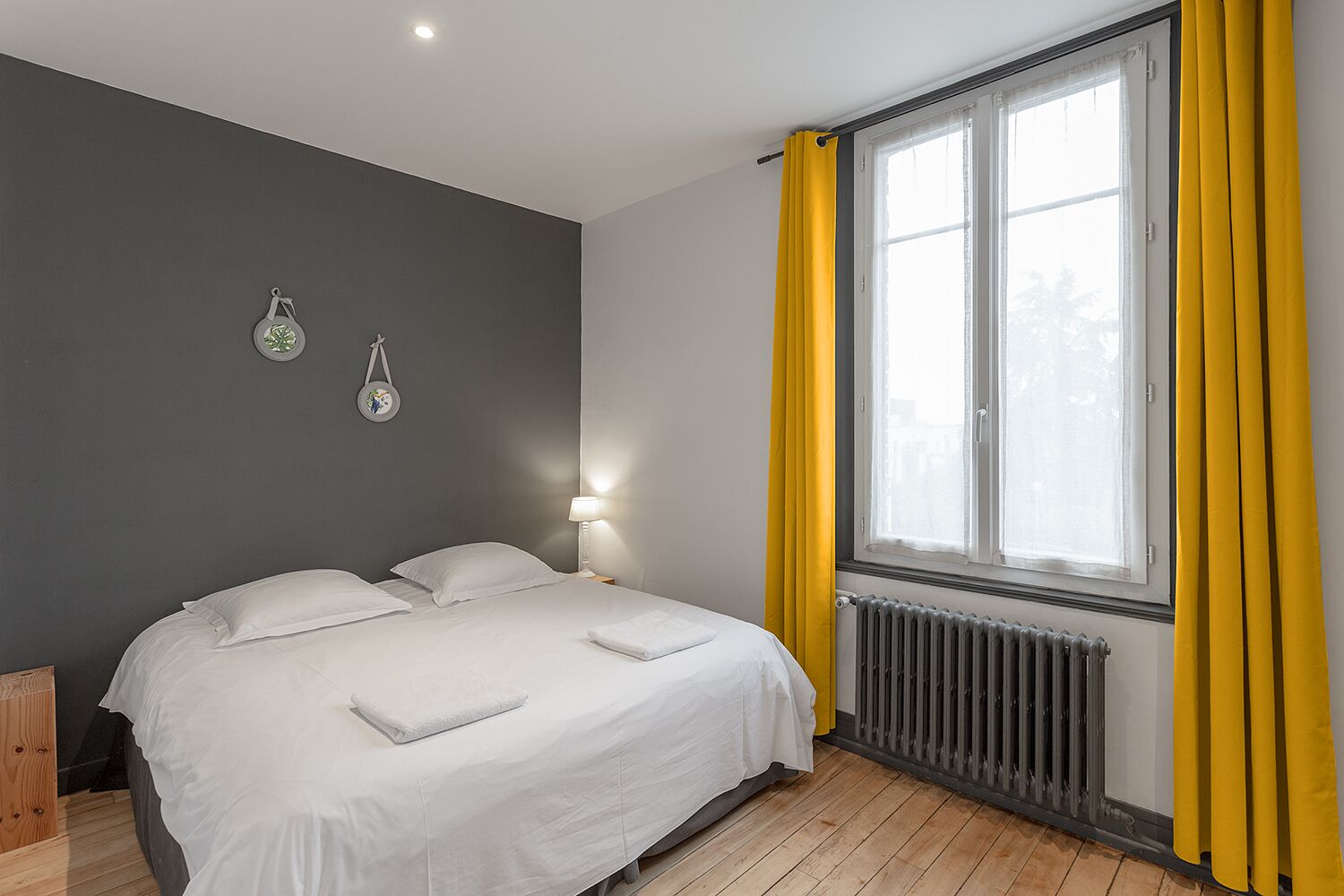 Ein Schlafzimmer mit einem Bett, zwei Wanduhren, einem Fenster mit gelben Vorhängen und einer Heizung.