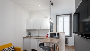 A compact kitchen with white cabinets, a microwave, and a sink. There is a yellow chair and a small table with stools.