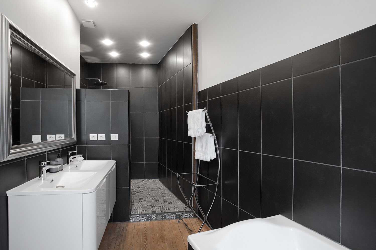 A modern bathroom with dark tiled walls, a white sink, a mirror, and a shower area.