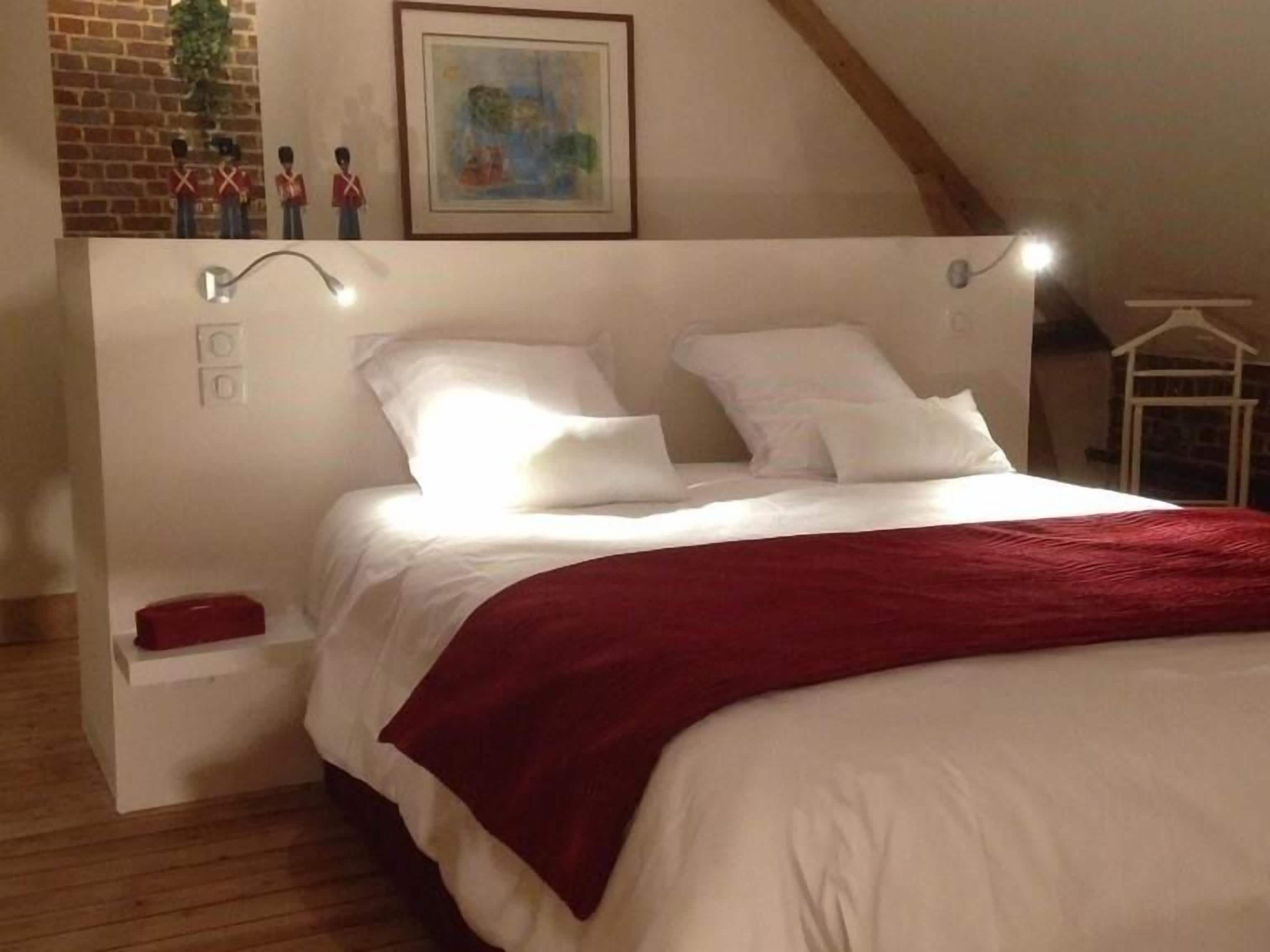 A bedroom with a large bed, a red throw blanket, a white headboard, and a painting above the bed.