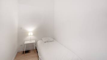 Una habitación pequeña con una cama individual, una mesita de noche y una lámpara.