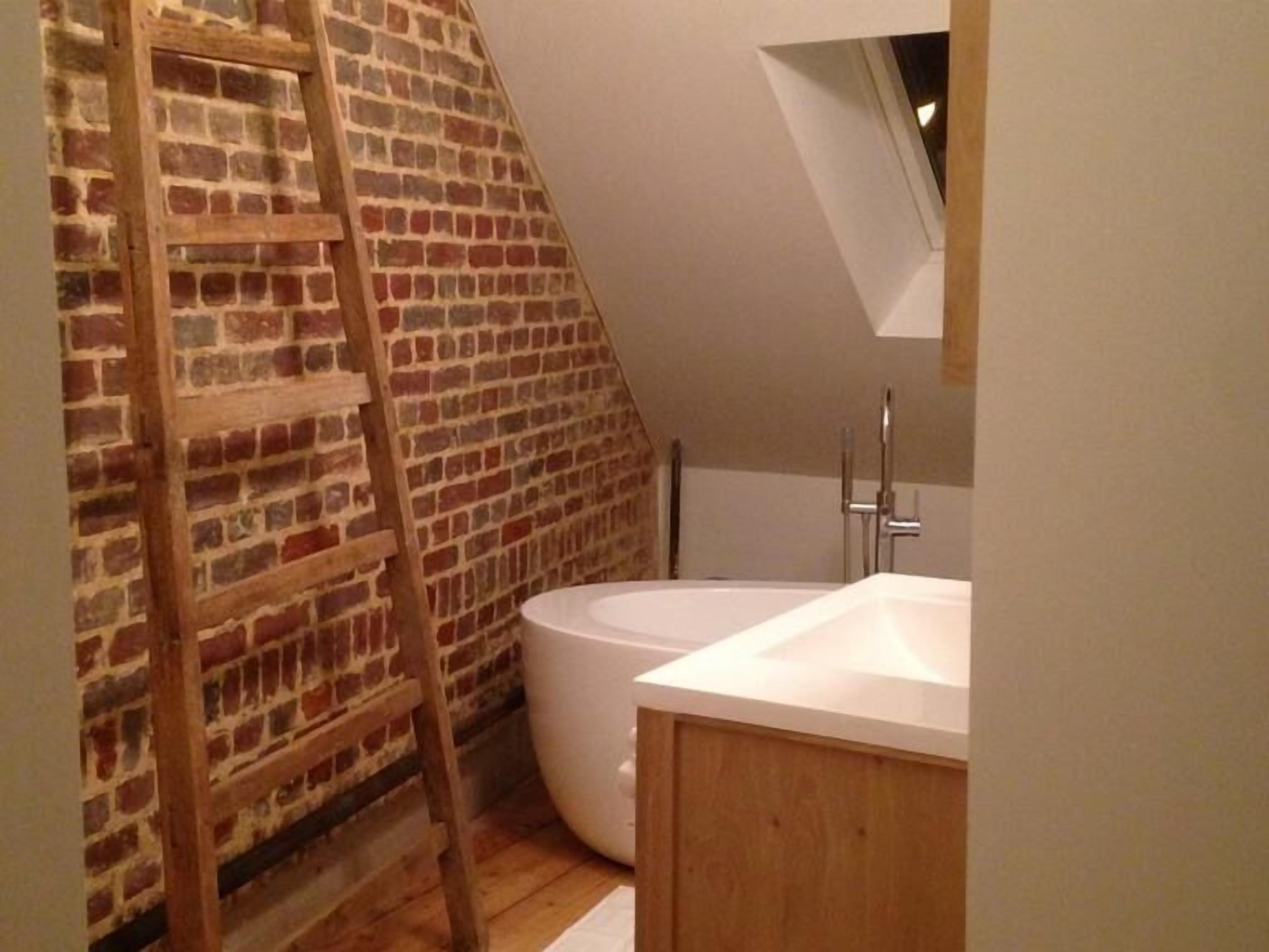 A bathroom with a brick wall, a wooden ladder, a white bathtub, and a wooden cabinet.