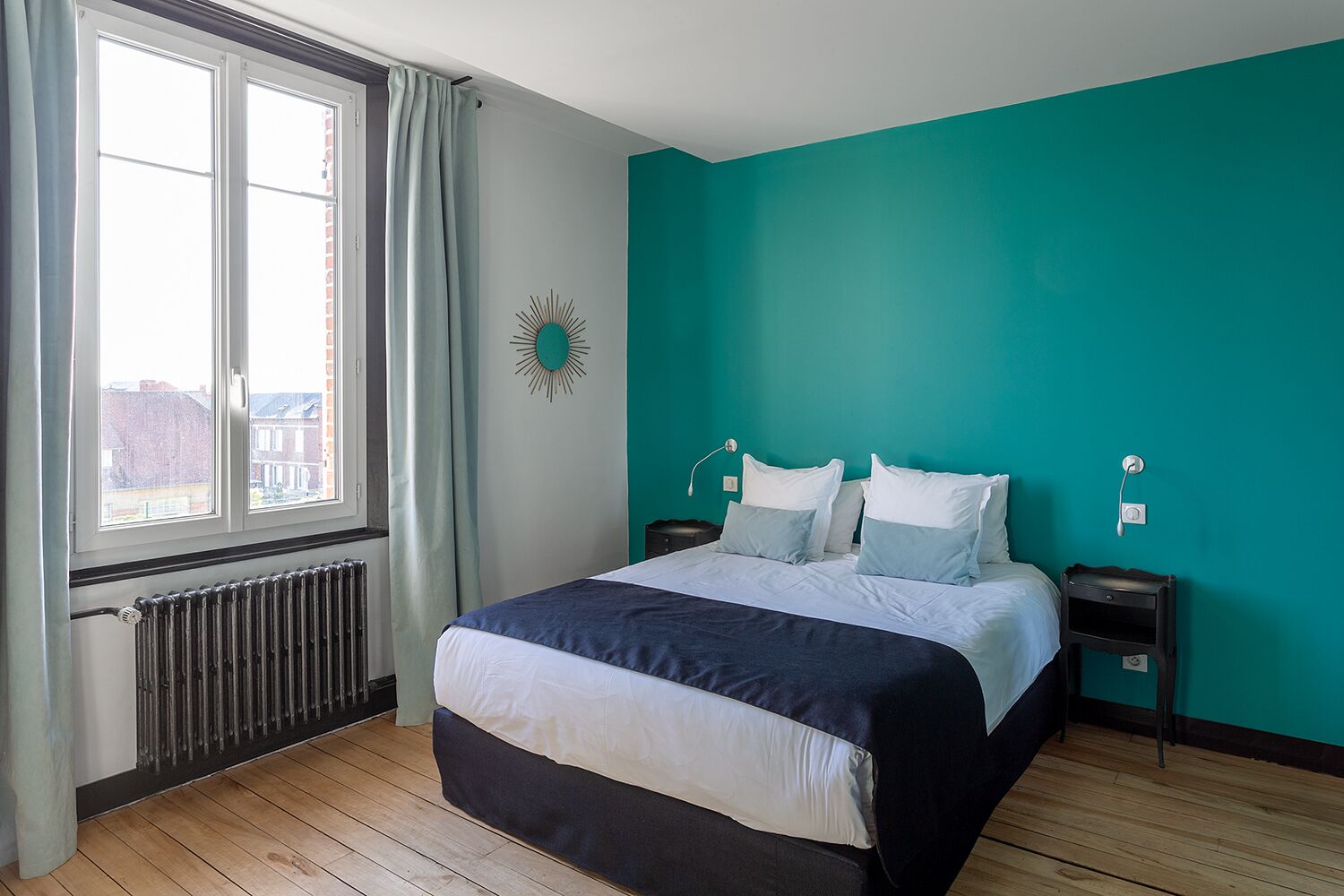 Une chambre à coucher avec un lit, une fenêtre, un radiateur, un mur de couleur turquoise et une horloge murale.