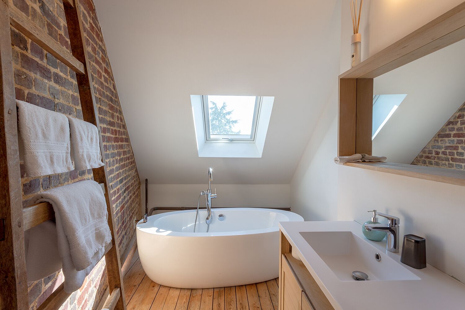 Een moderne badkamer met een vrijstaand bad, dakraam en een houten vloer.