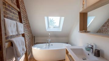 Een moderne badkamer met een vrijstaand bad, dakraam en een houten vloer.