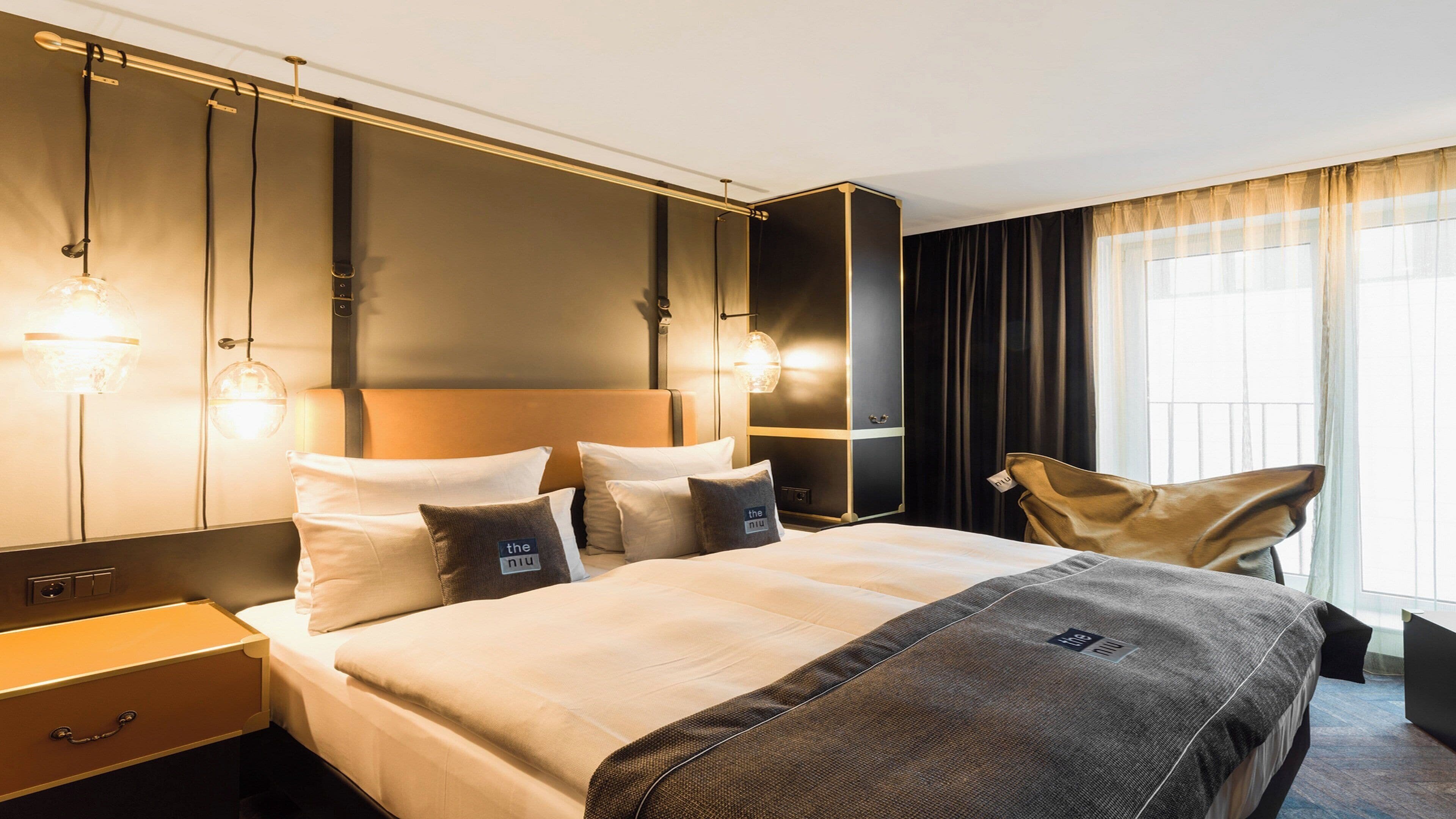 Ein modernes Hotelzimmer mit einem großen Bett, Nachttischen, einem Kleiderschrank und einem großen Fenster mit Vorhängen.