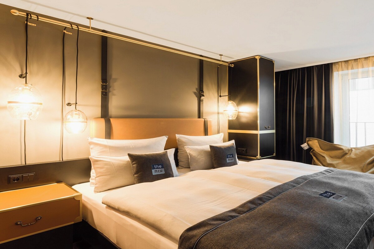 Ein modernes Hotelzimmer mit einem großen Bett, Nachttischen, einem Kleiderschrank und einem großen Fenster mit Vorhängen.
