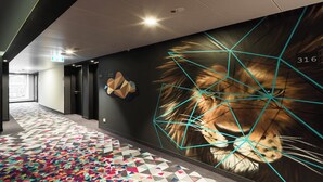 A hallway with a geometric patterned carpet, a large lion mural, and a number '316' on the wall. - Holiday Inn - the niu, Cobbles Essen by IHG (Essen)