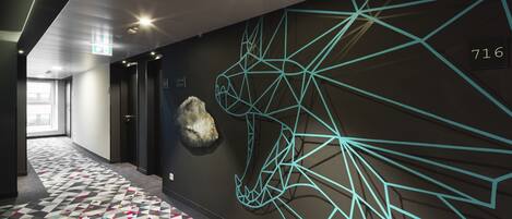 A hallway with a geometric patterned floor, a wall-mounted sculpture, and a ceiling with a geometric light design.
