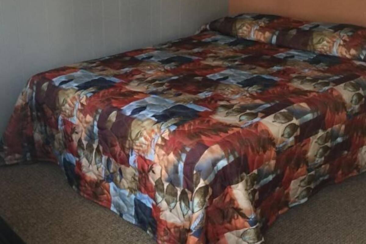 Una cama con un colcha colorida en una habitación de paredes lisas y piso alfombrado.