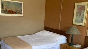 Quarto de hotel com duas camas, uma mesa de cabeceira com abajur, e duas molduras nas paredes.