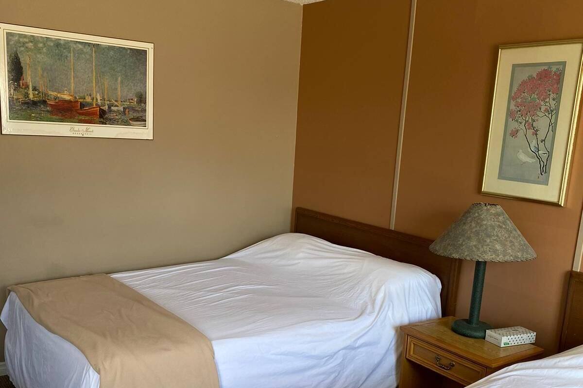 Una habitación de hotel con dos camas, una mesita de noche con una lámpara, y dos cuadros en las paredes.