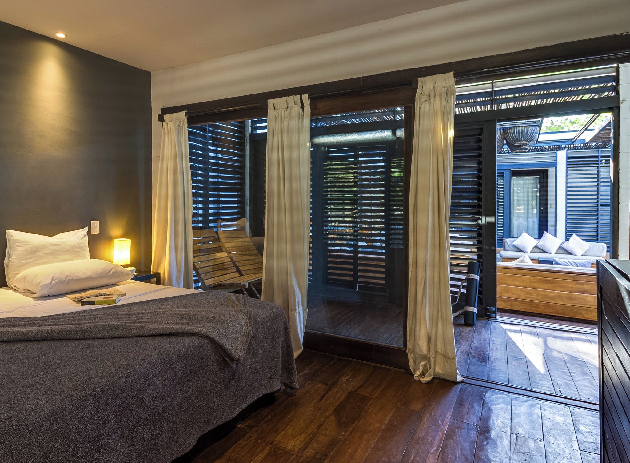 A modern bedroom with a bed, bedside lamp, and a view of an outdoor seating area through a sliding door.